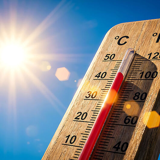 Symbolic image shows wooden thermometer against a blue sky and bright sun, reading about 40 degrees Celsius.