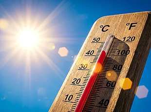 Symbolbild zeigt Holzthermometer vor blauem Himmel und strahlender Sonne; die Temperatur liegt bei etwa 40 Grad Celsius.