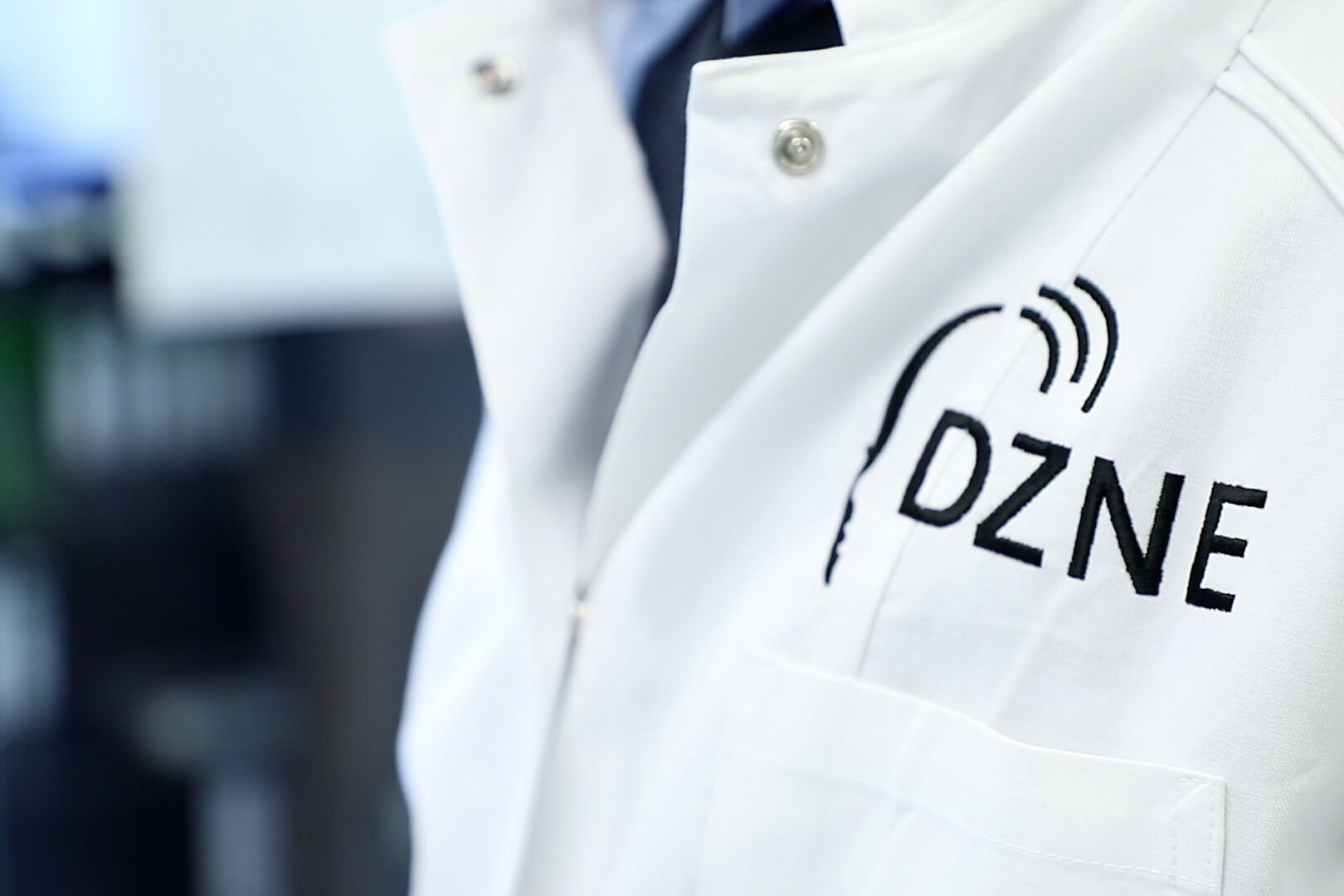 Bild zeigt Laborkittel mit DZNE-Logo.
