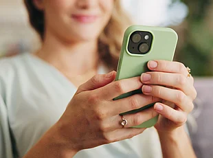 Nahaufnahme einer Person, die ein Smartphone mit grüner Hülle in beiden Händen hält und auf den Bildschirm blickt