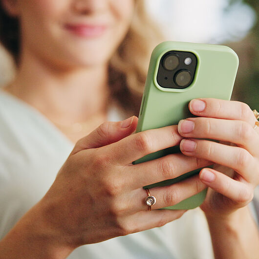 Nahaufnahme einer Person, die ein Smartphone mit grüner Hülle in beiden Händen hält und auf den Bildschirm blickt