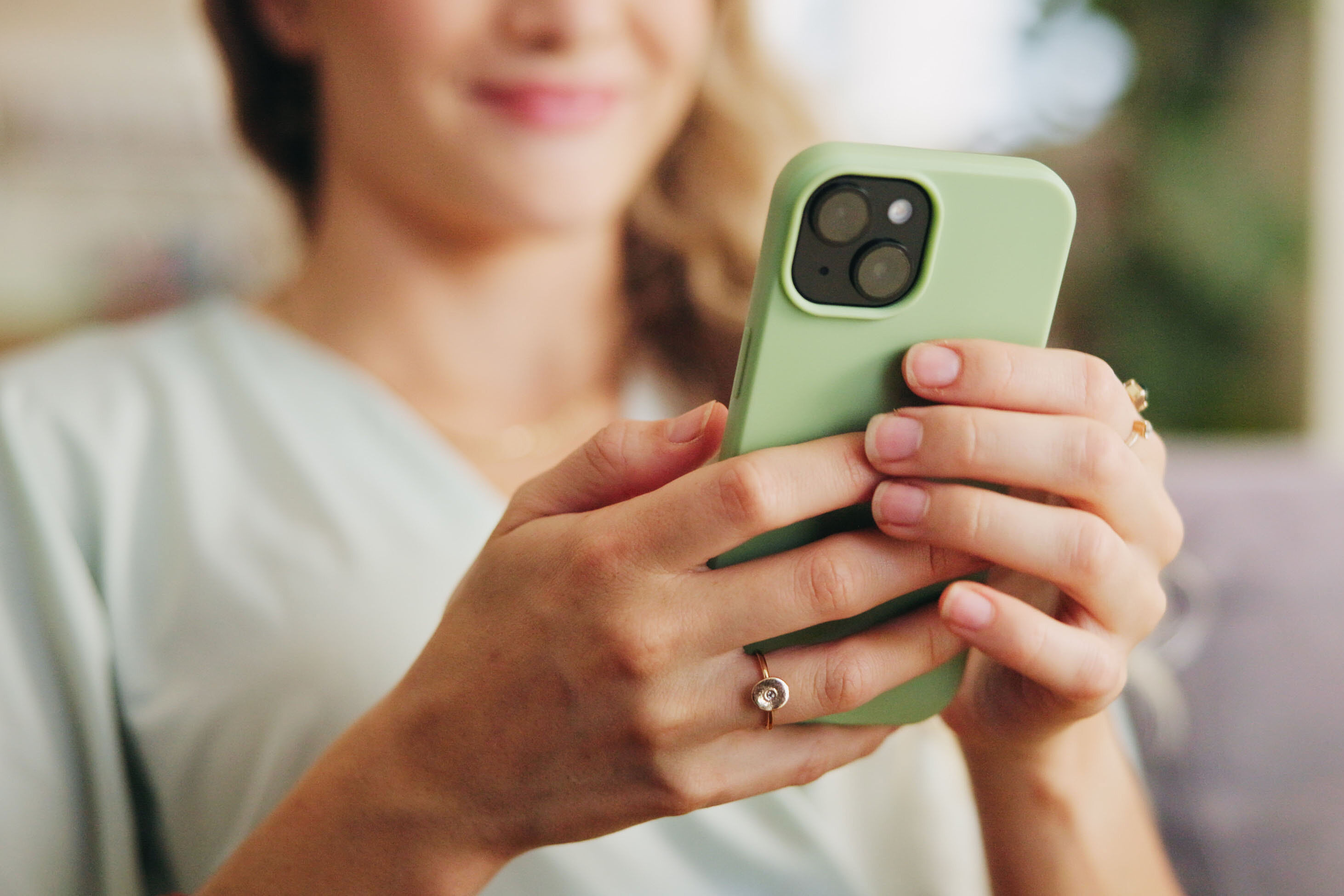 Nahaufnahme einer Person, die ein Smartphone mit grüner Hülle in beiden Händen hält und auf den Bildschirm blickt
