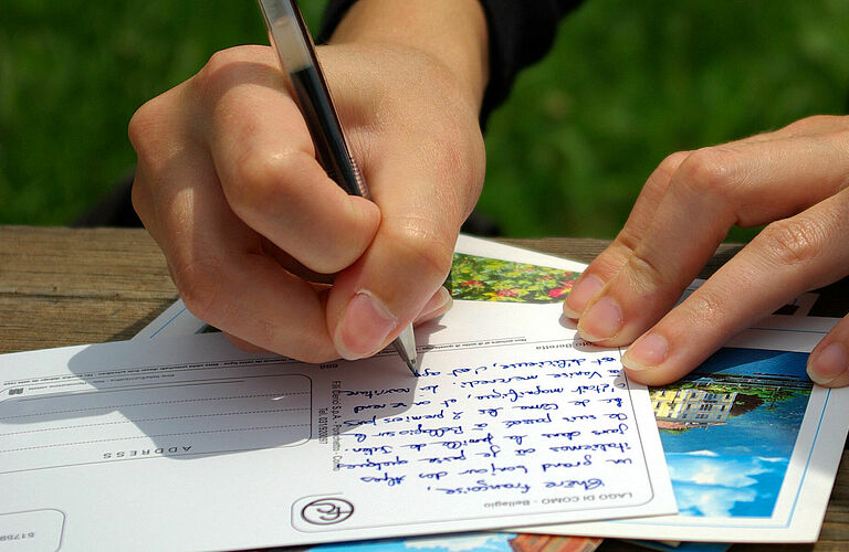 Bild zeigt Postkarte mit schreibender Hand.