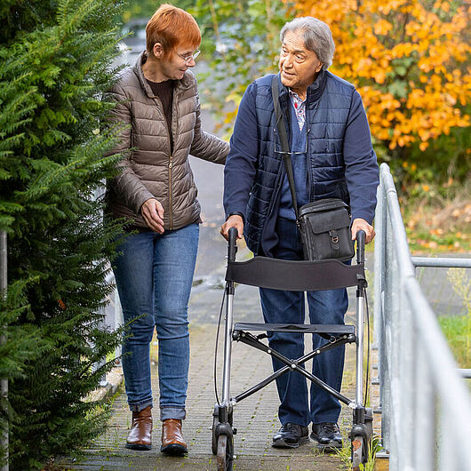 Picture shows a care worker with an elderly gentleman on a rollator.